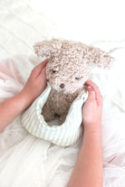 Person holding a small dog-shaped pillow with fluffy texture on a soft white background