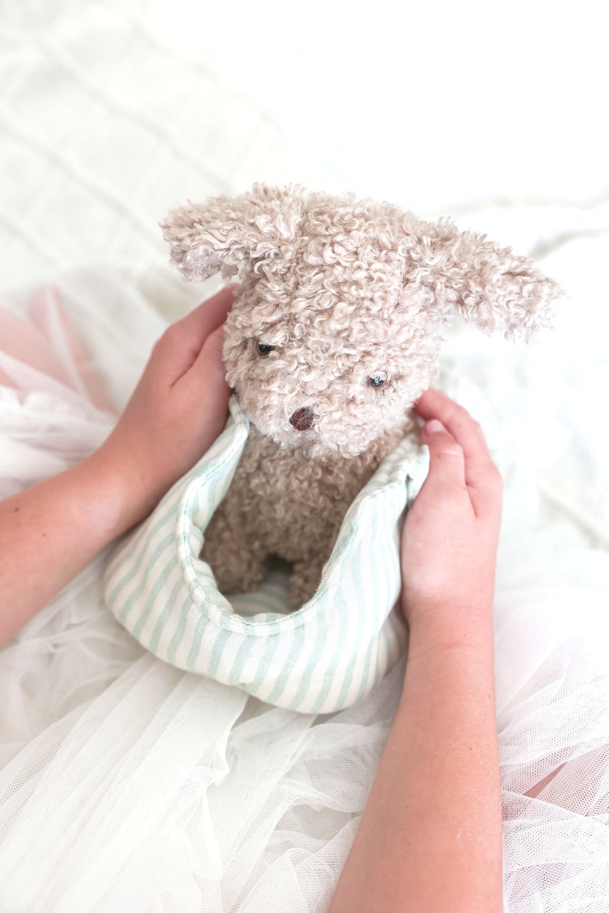 Person holding a small dog-shaped pillow with fluffy texture on a soft white background