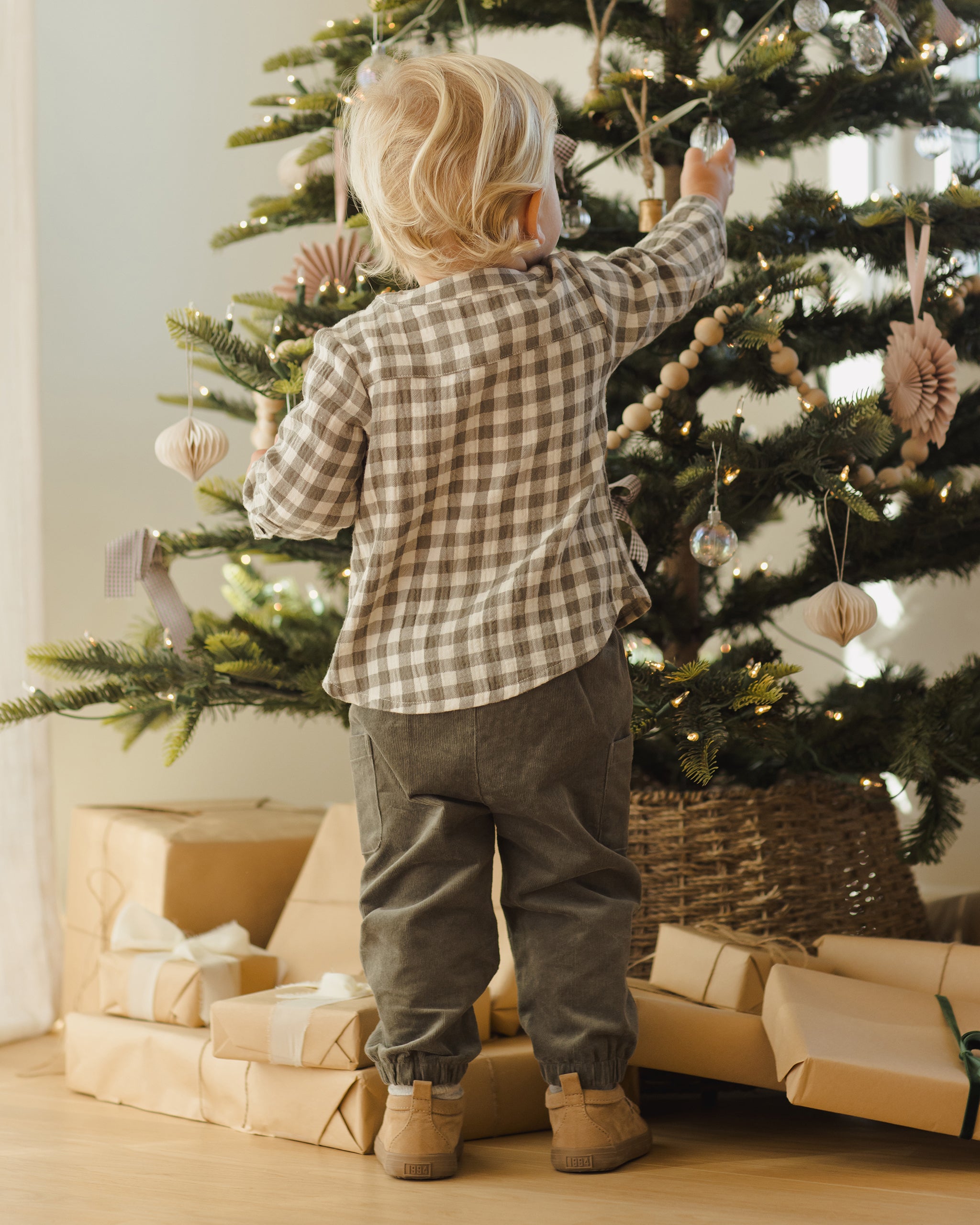 Child decorating a Christmas tree with ornaments, surrounded by wrapped gifts.