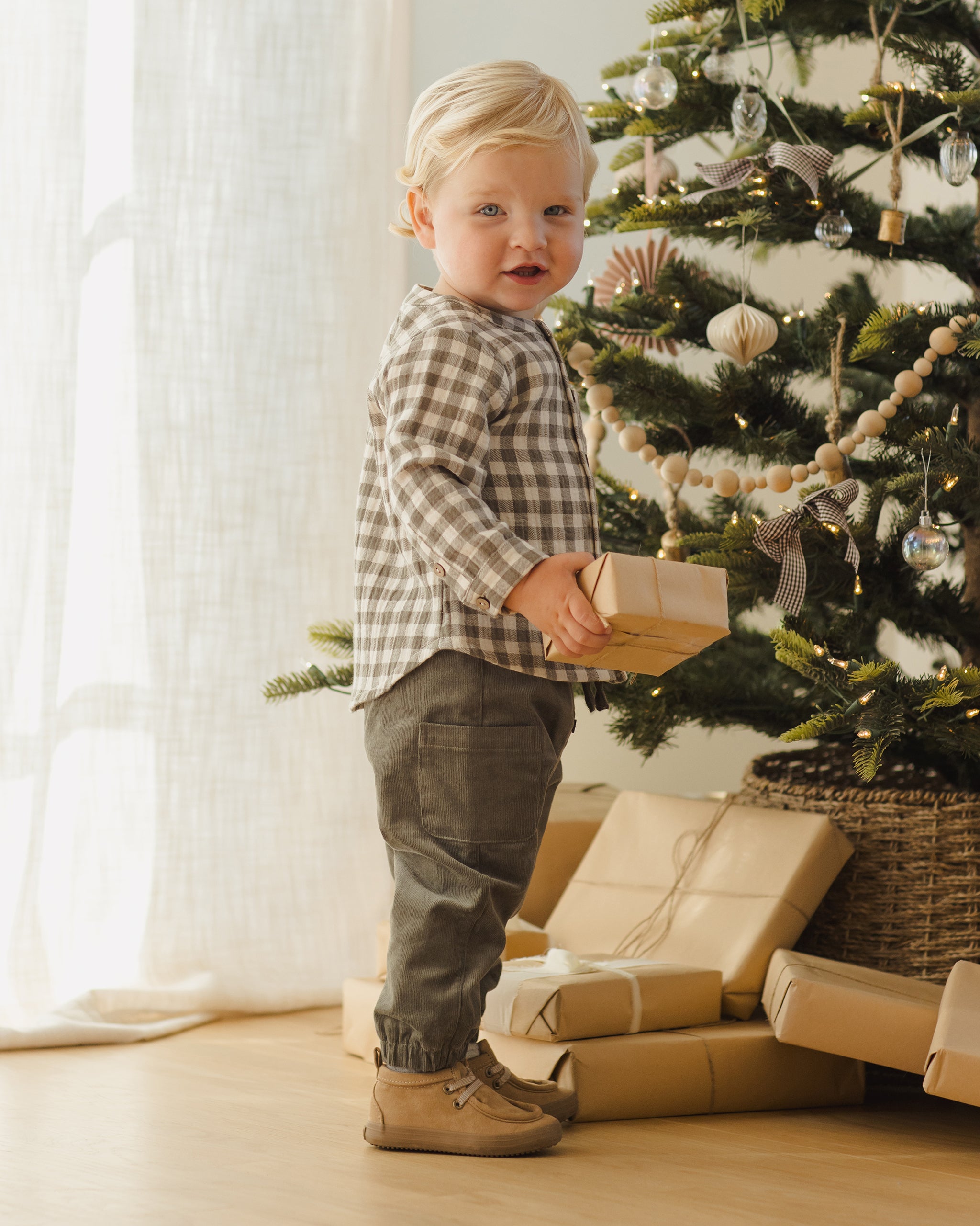 Child standing next to a decorated Christmas tree with presents underneath.