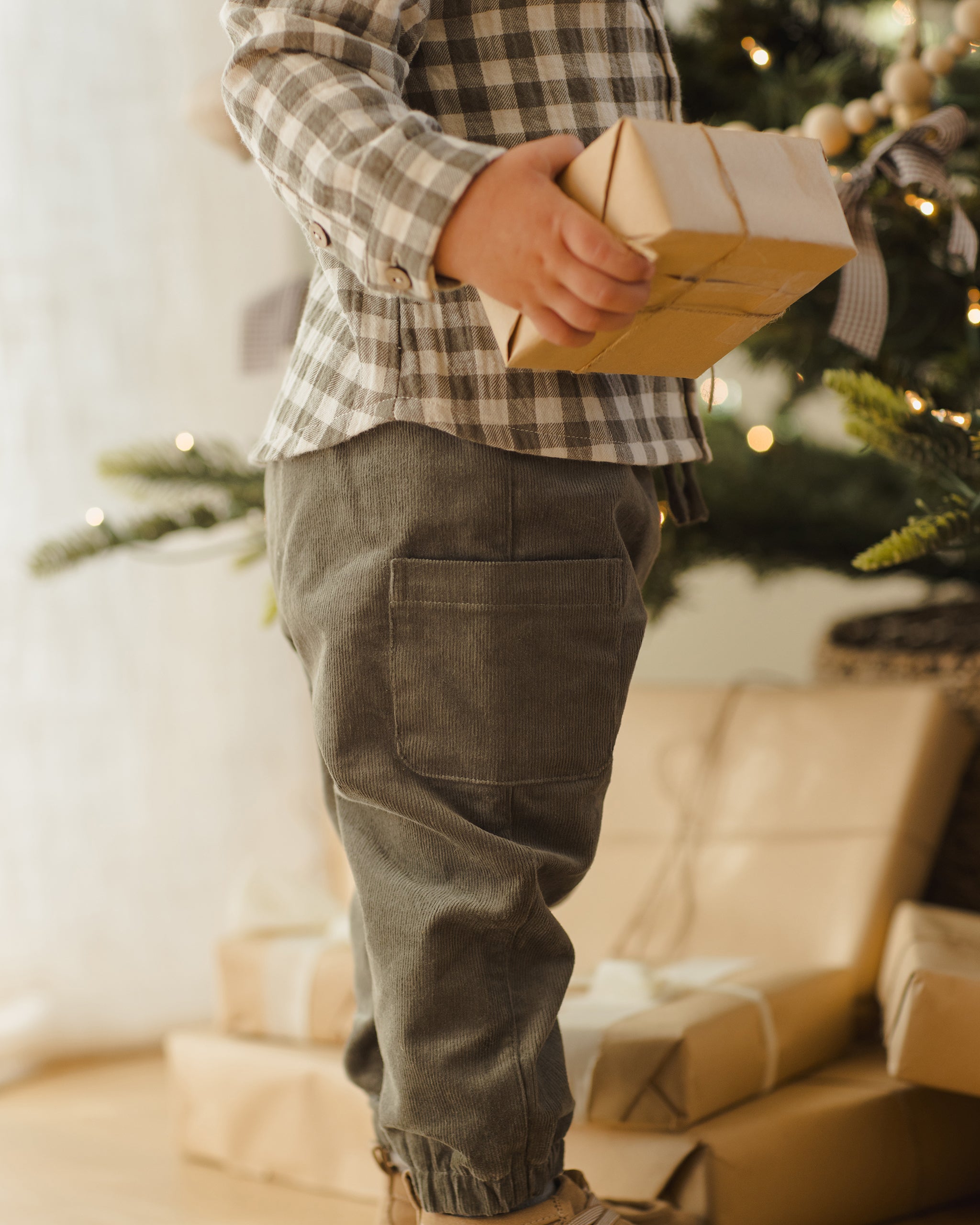Child holding a gift box in front of a decorated Christmas tree.