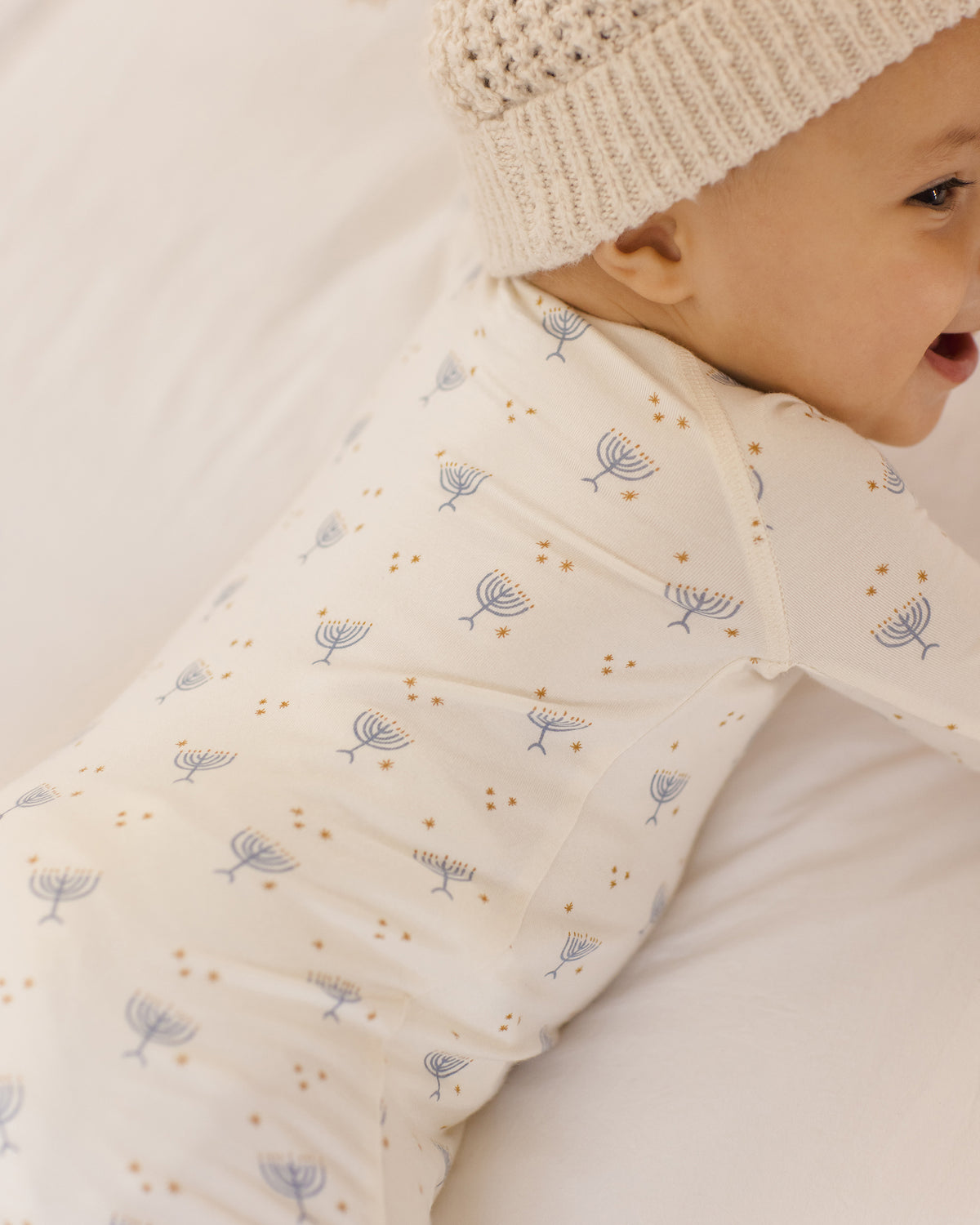 Baby wearing a cream-colored sleeping bag with subtle patterns and a matching hat.