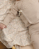 A close-up of a baby wearing a beige and white striped long-sleeve romper, lying on a matching beige and white floral blanket.