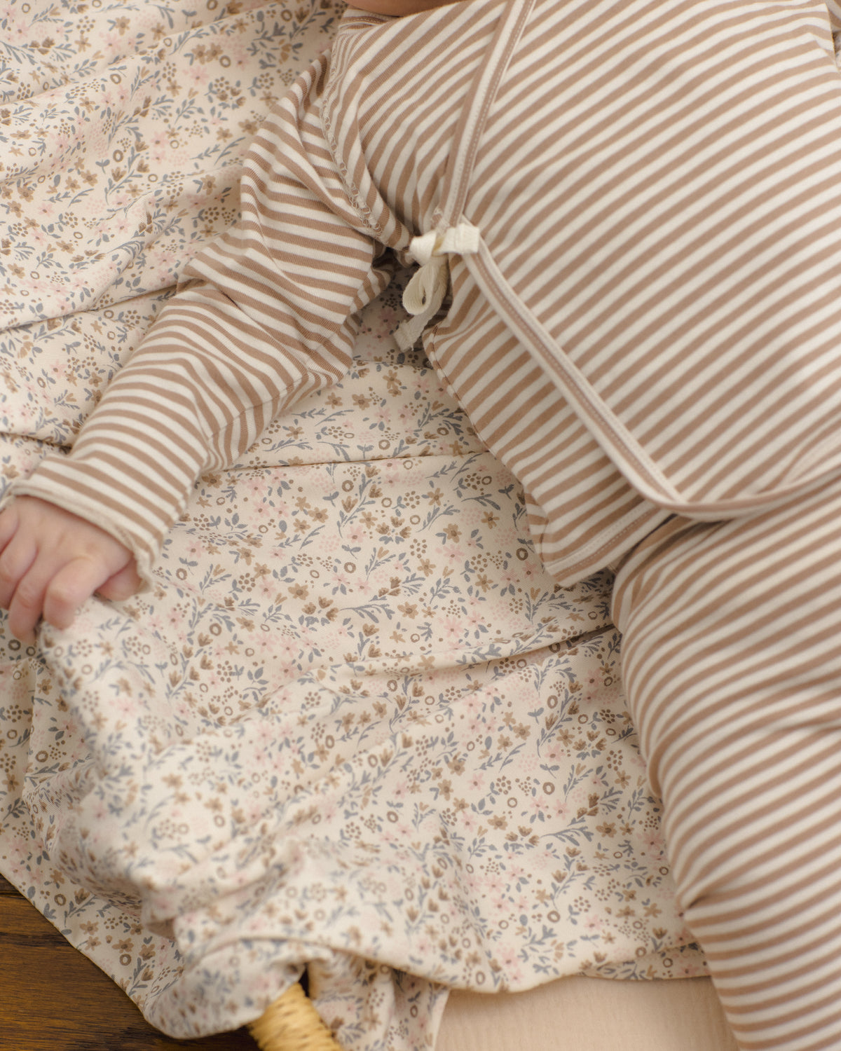 A close-up of a baby wearing a beige and white striped long-sleeve romper, lying on a matching beige and white floral blanket.