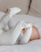 A baby lying on a white bed, wearing a long-sleeve footed sleeper with thin gray and white stripes.