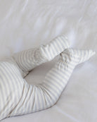 A close-up of a baby's legs wearing soft, cream-colored footed socks or booties with thin gray stripes, resting on white bedding.