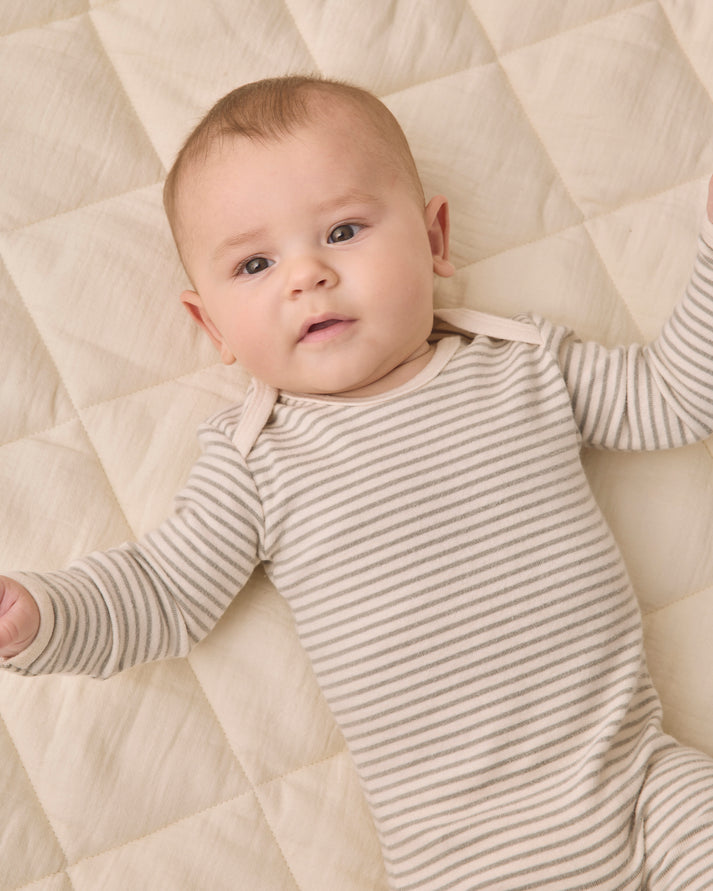 A baby lying on a quilted cream mattress, wearing a beige and white horizontally striped long-sleeve bodysuit.
