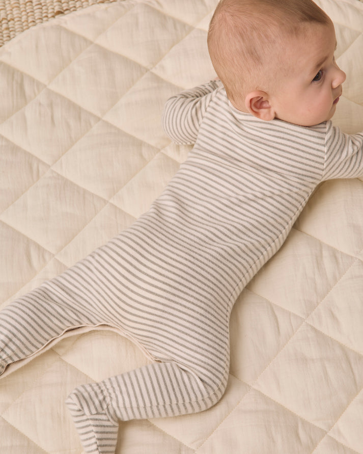 A baby lying on their stomach wearing a cream and beige striped footed sleeper, lying on a quilted cream blanket.