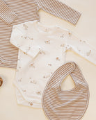 A baby clothing flat lay featuring a long-sleeve bodysuit in off-white with tiny brown animal prints, a matching striped long-sleeve top in beige and brown, and a striped bib.