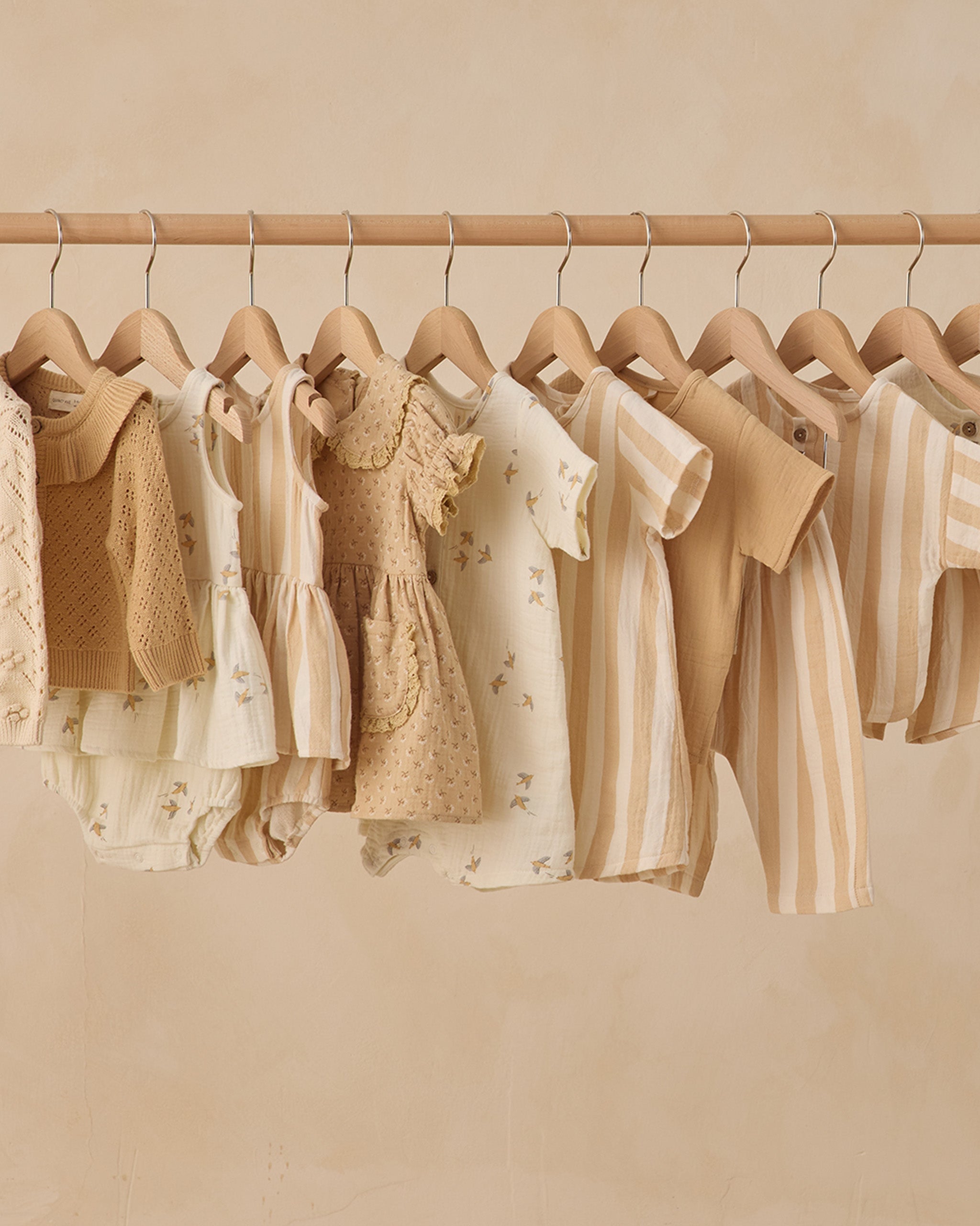 Row of children's clothing on hangers against a beige wall