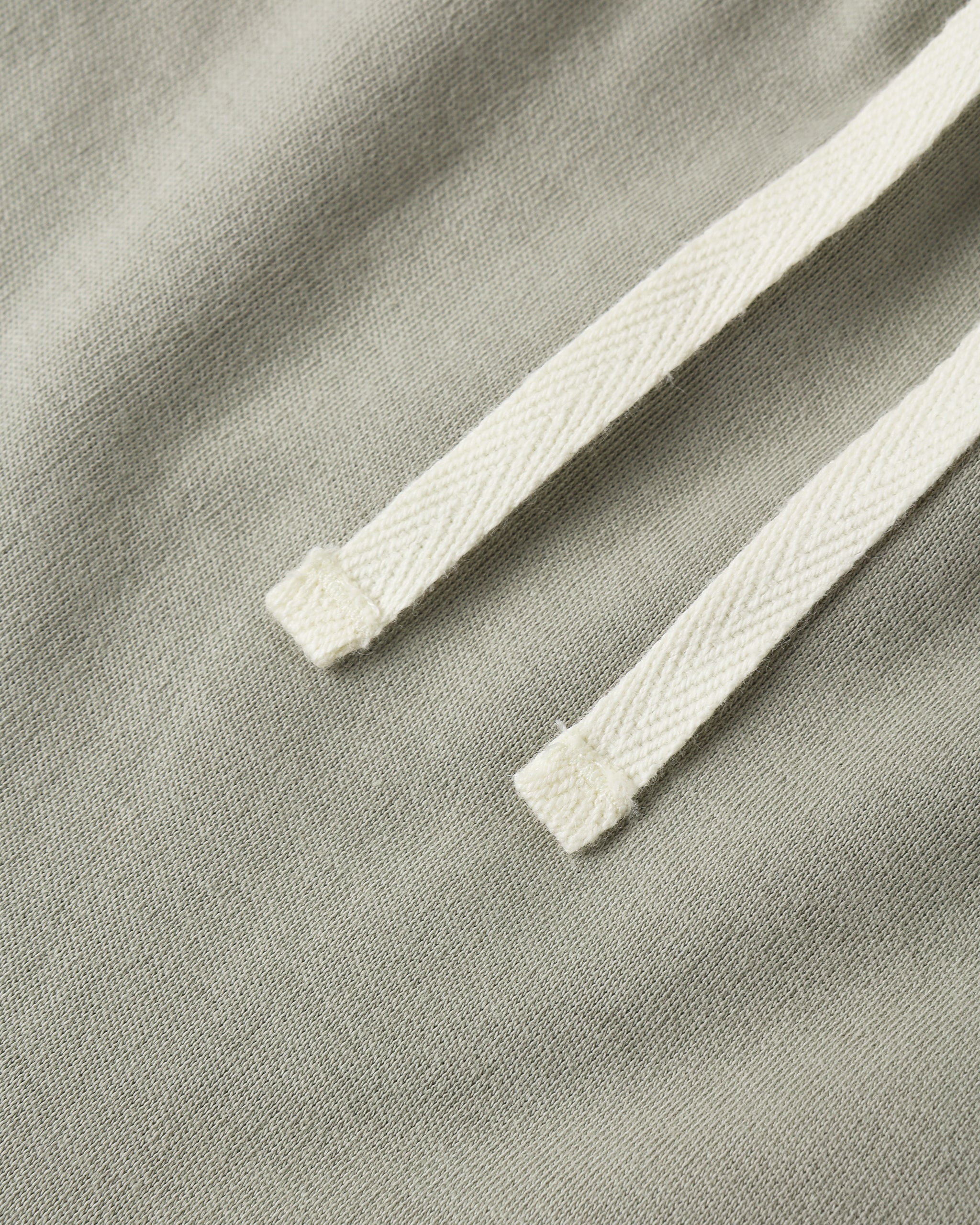 Close-up of a light sage green fabric with a contrasting off-white braided drawstring.