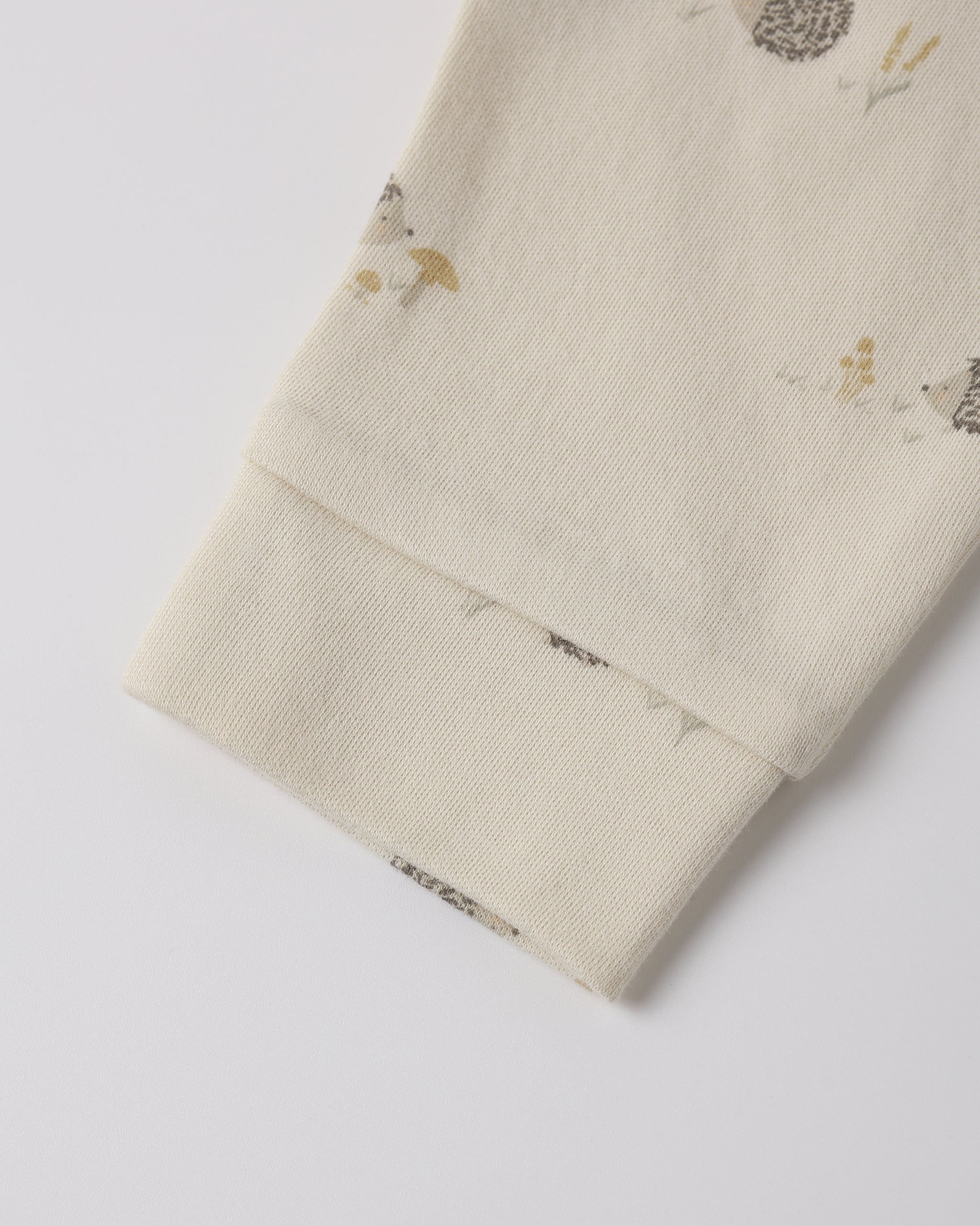 Close-up of a cream-colored fabric sleeve or cuff with a small woodland print of hedgehogs, mushrooms, and birds, finished with a ribbed elastic cuff.