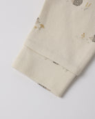 Close-up of a cream-colored fabric sleeve or cuff with a small woodland print of hedgehogs, mushrooms, and birds, finished with a ribbed elastic cuff.