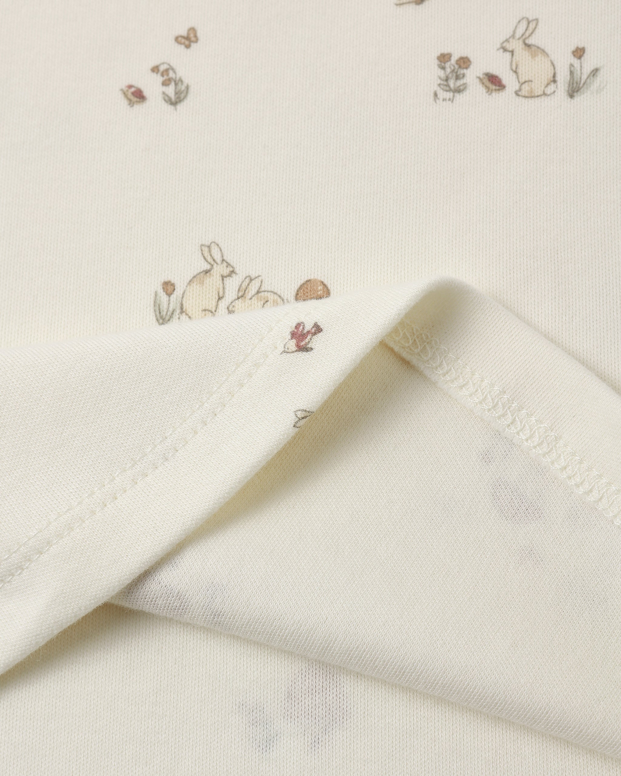 Close-up of a cream-colored fabric with a delicate bunny and floral print, showing the soft texture and folded hem.