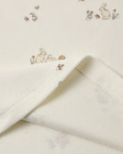Close-up of a cream-colored fabric with a delicate bunny and floral print, showing the soft texture and folded hem.