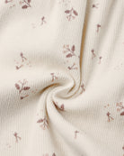 A close-up of cream-colored ribbed fabric with a delicate, small-scale dusty rose floral print, styled with a central swirl to show texture and drape.