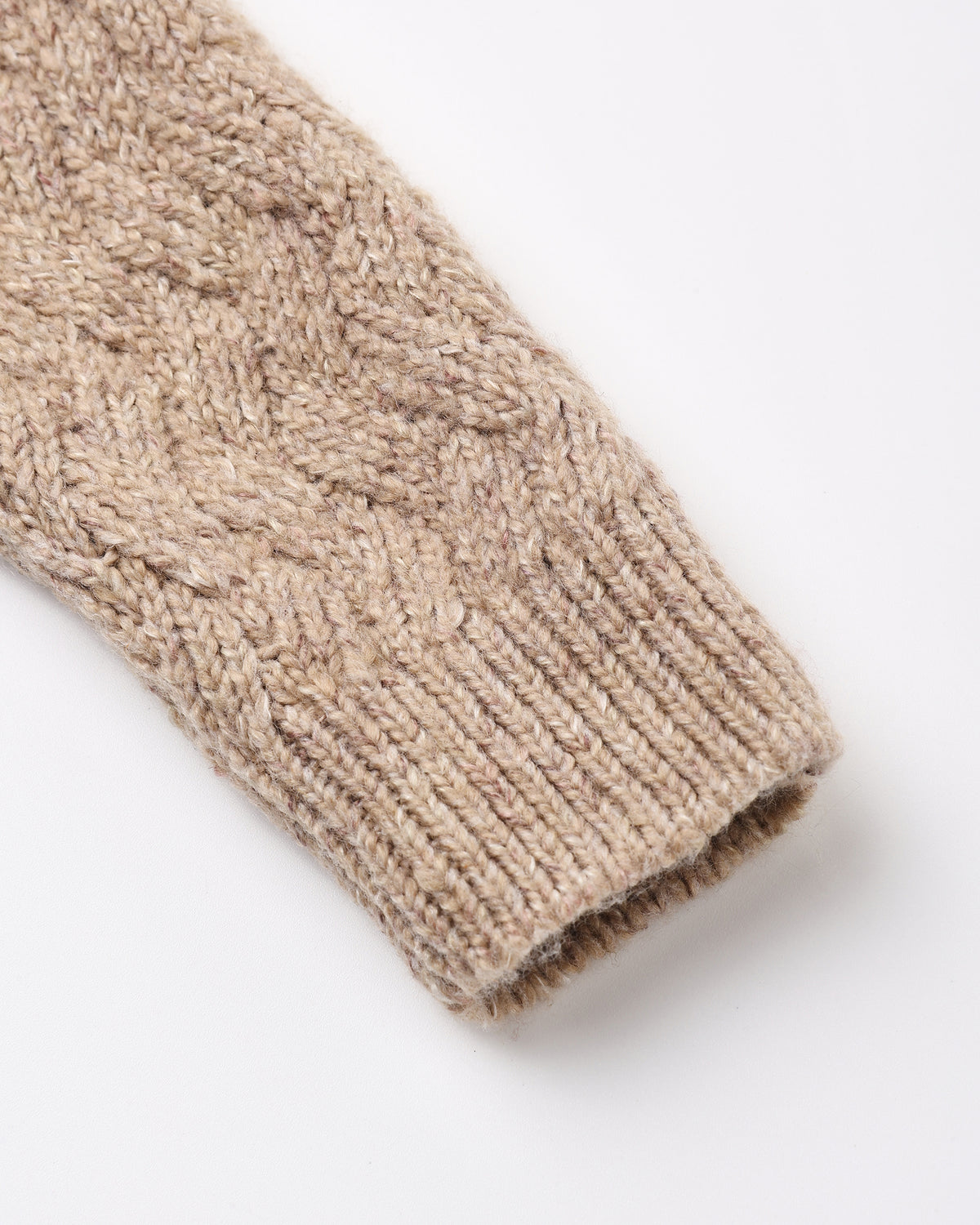 Close-up of a beige cable-knit sweater sleeve with a ribbed cuff, shown on a plain white background.