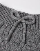 Close-up of a gray cable-knit garment with a ribbed neckline and a knotted bow detail at the center front.