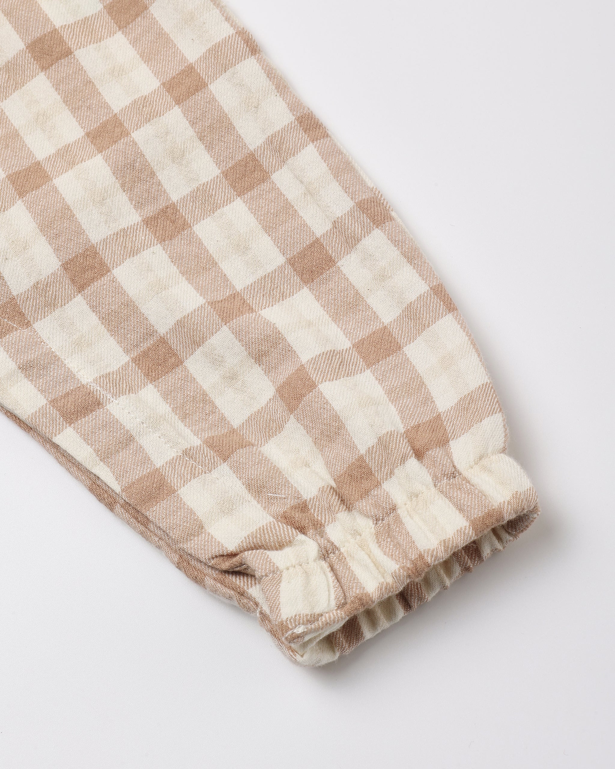 A close-up of a beige and off-white gingham checkered fabric item, showing a gathered elastic cuff on a light gray background.