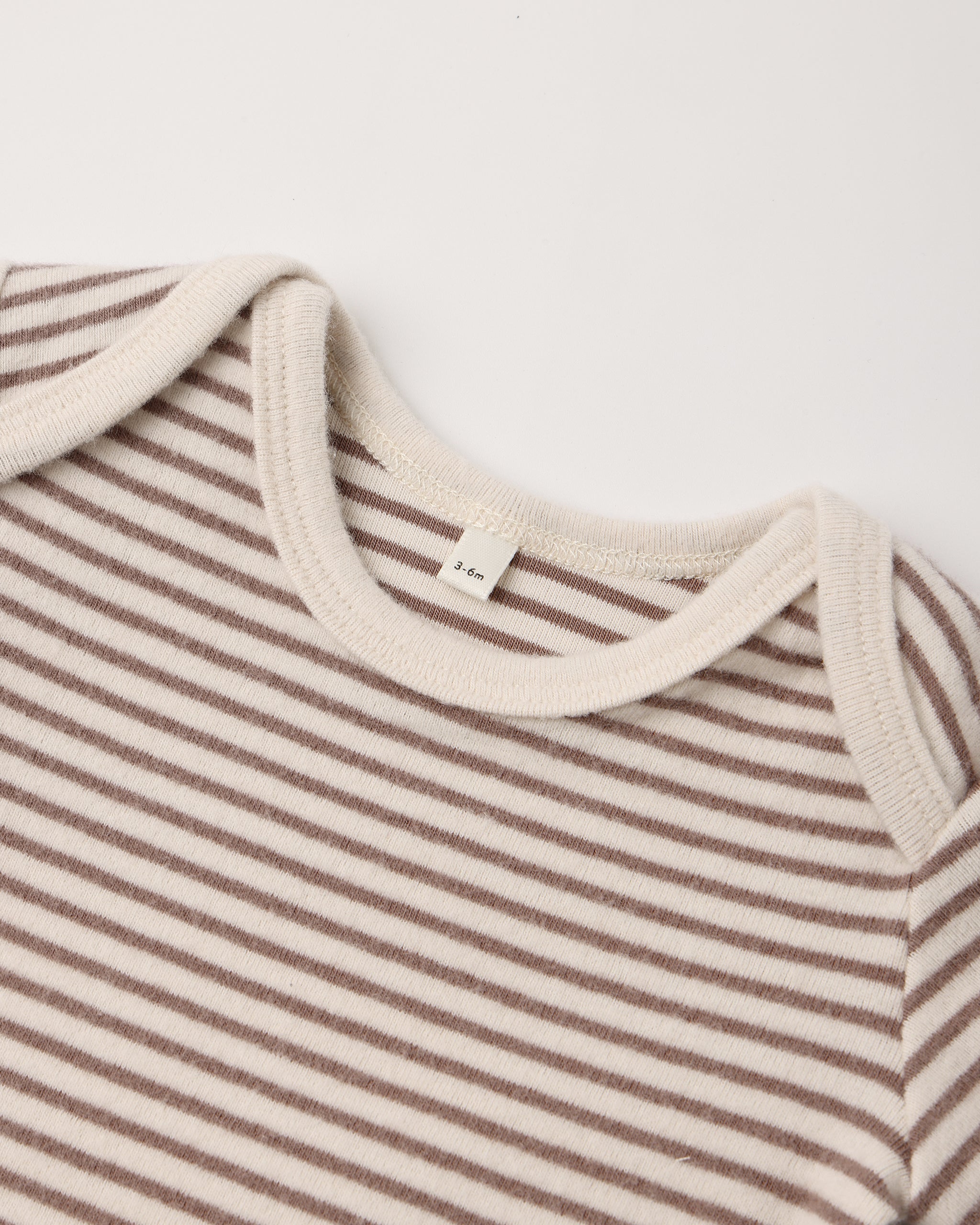 Close-up of a baby long-sleeve top with thin brown and cream horizontal stripes, featuring a ribbed cream crew neck and shoulder yokes.