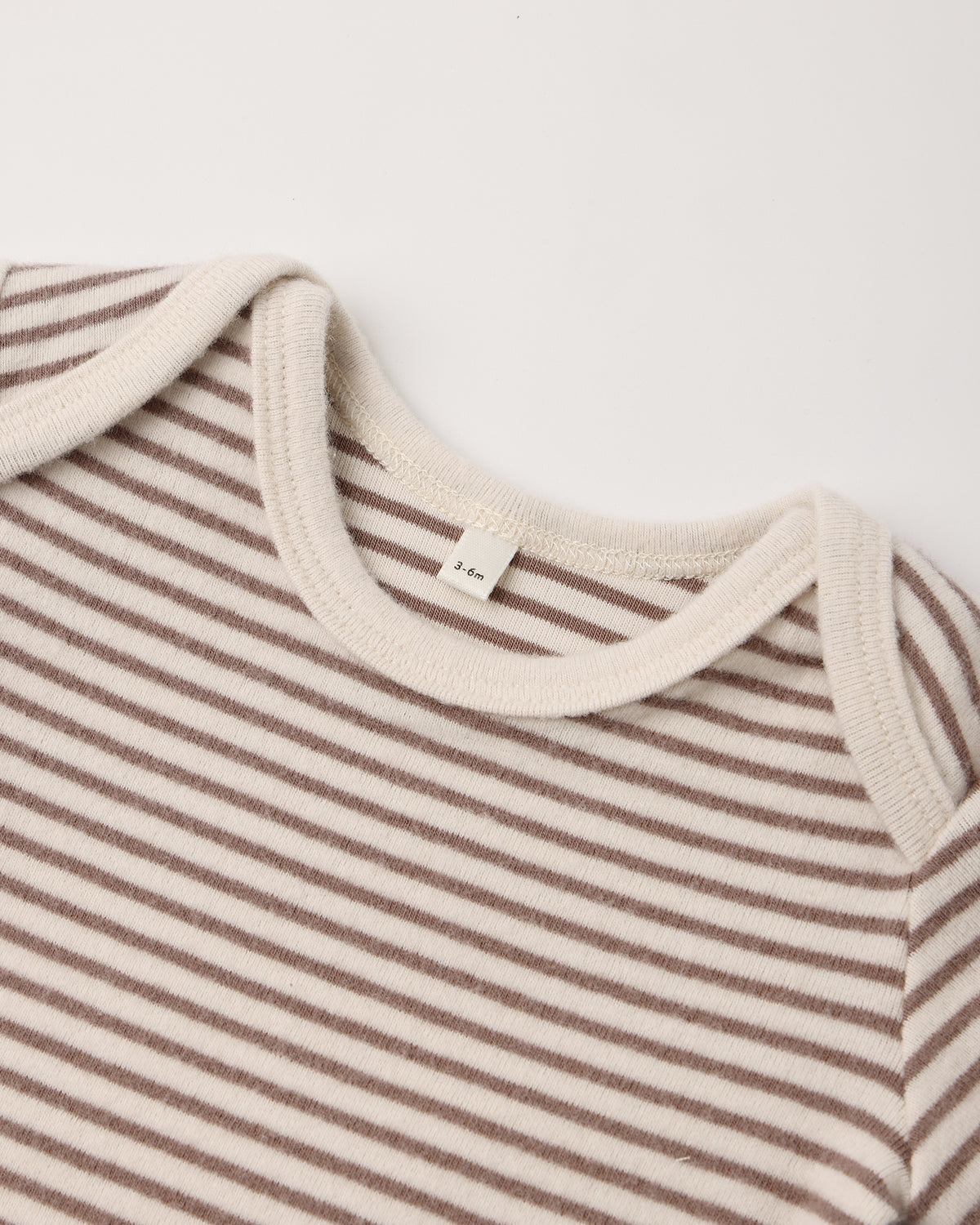 Close-up of a baby long-sleeve top with thin brown and cream horizontal stripes, featuring a ribbed cream crew neck and shoulder yokes.
