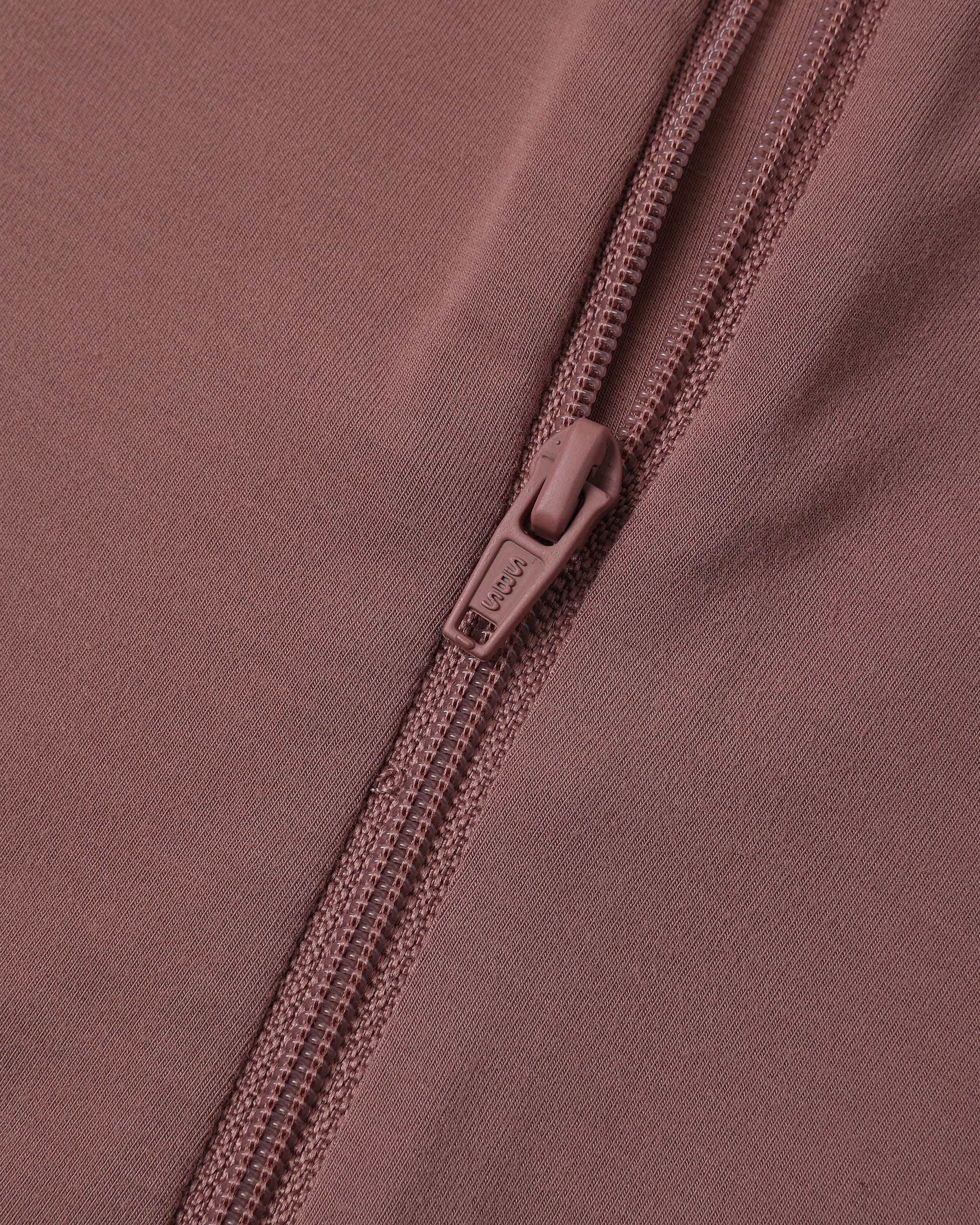 Close-up of a dusty rose pink zippered garment, showing the fabric texture and a matching pull tab with the brand name 'SOL'S' visible.