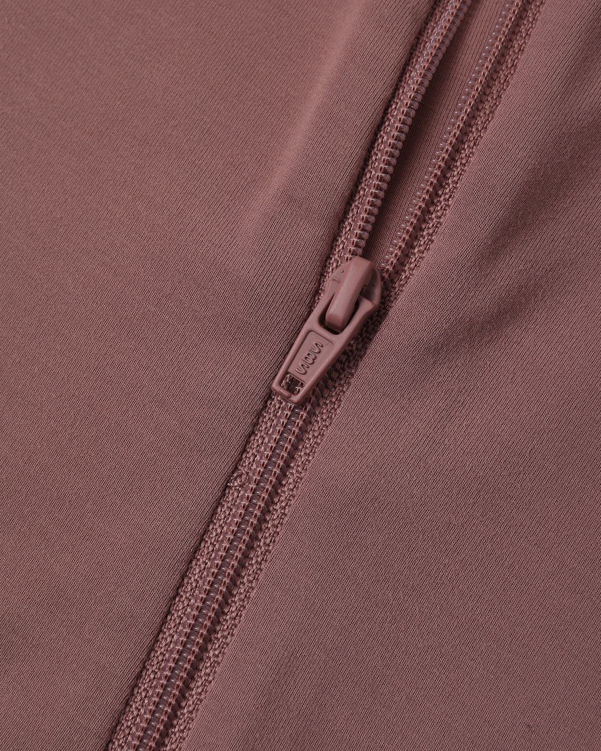Close-up of a dusty rose pink zippered garment, showing the fabric texture and a matching pull tab with the brand name 'SOL'S' visible.