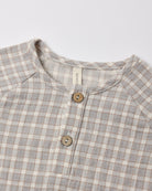 Close-up of a children's long-sleeve henley shirt with a light gray and beige gingham check pattern, featuring a button placket with wooden buttons and a visible neck label reading 'gugu'.