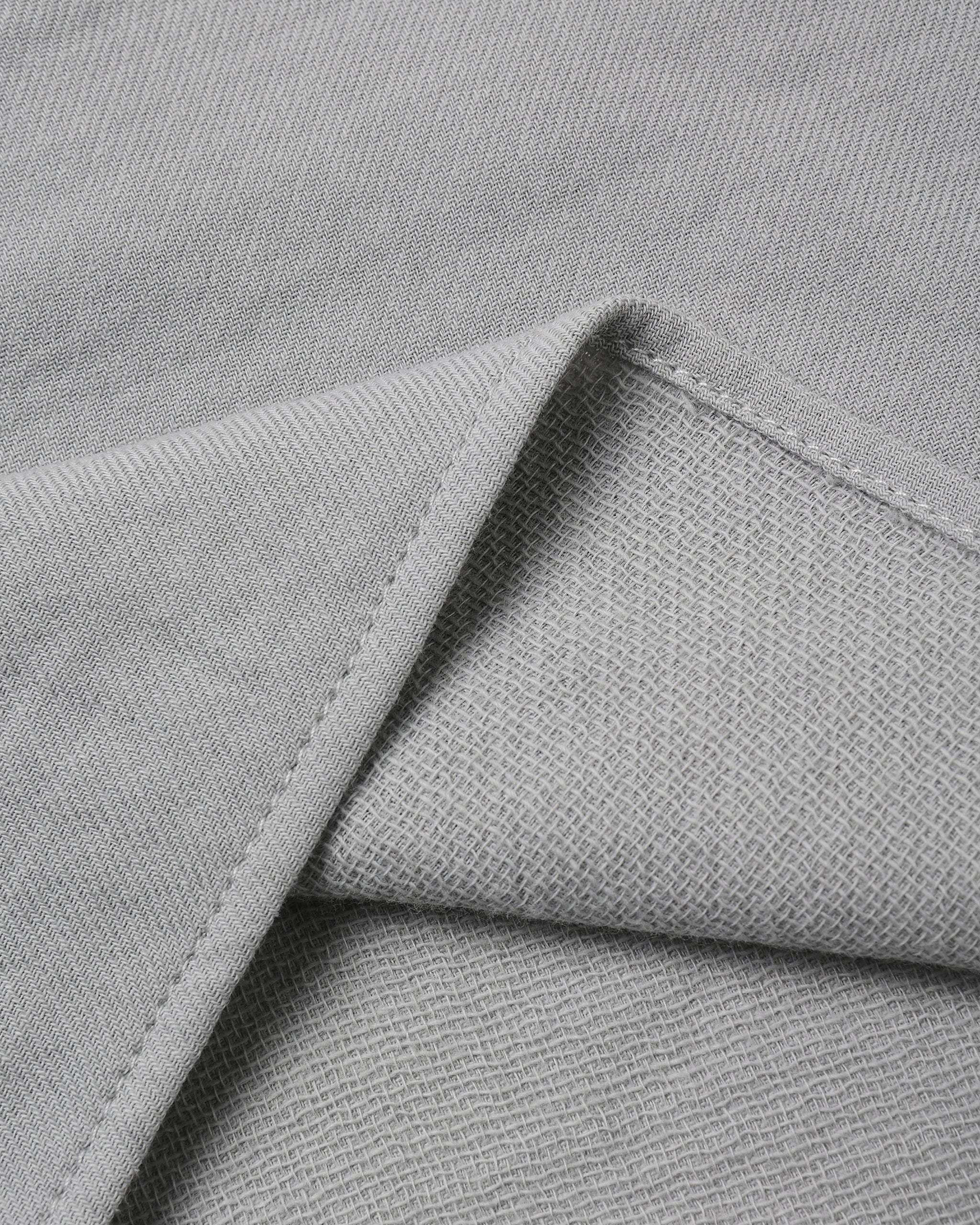 Close-up of light gray woven fabric with a folded corner showing the texture and stitching.