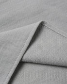 Close-up of light gray woven fabric with a folded corner showing the texture and stitching.