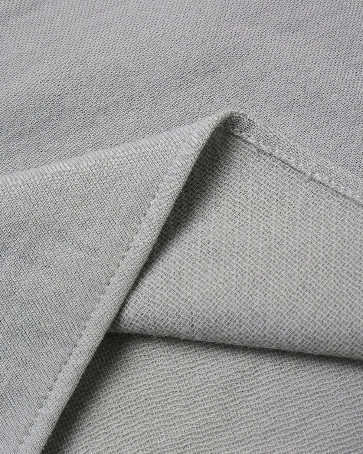 Close-up of light gray woven fabric with a folded corner showing the texture and stitching.