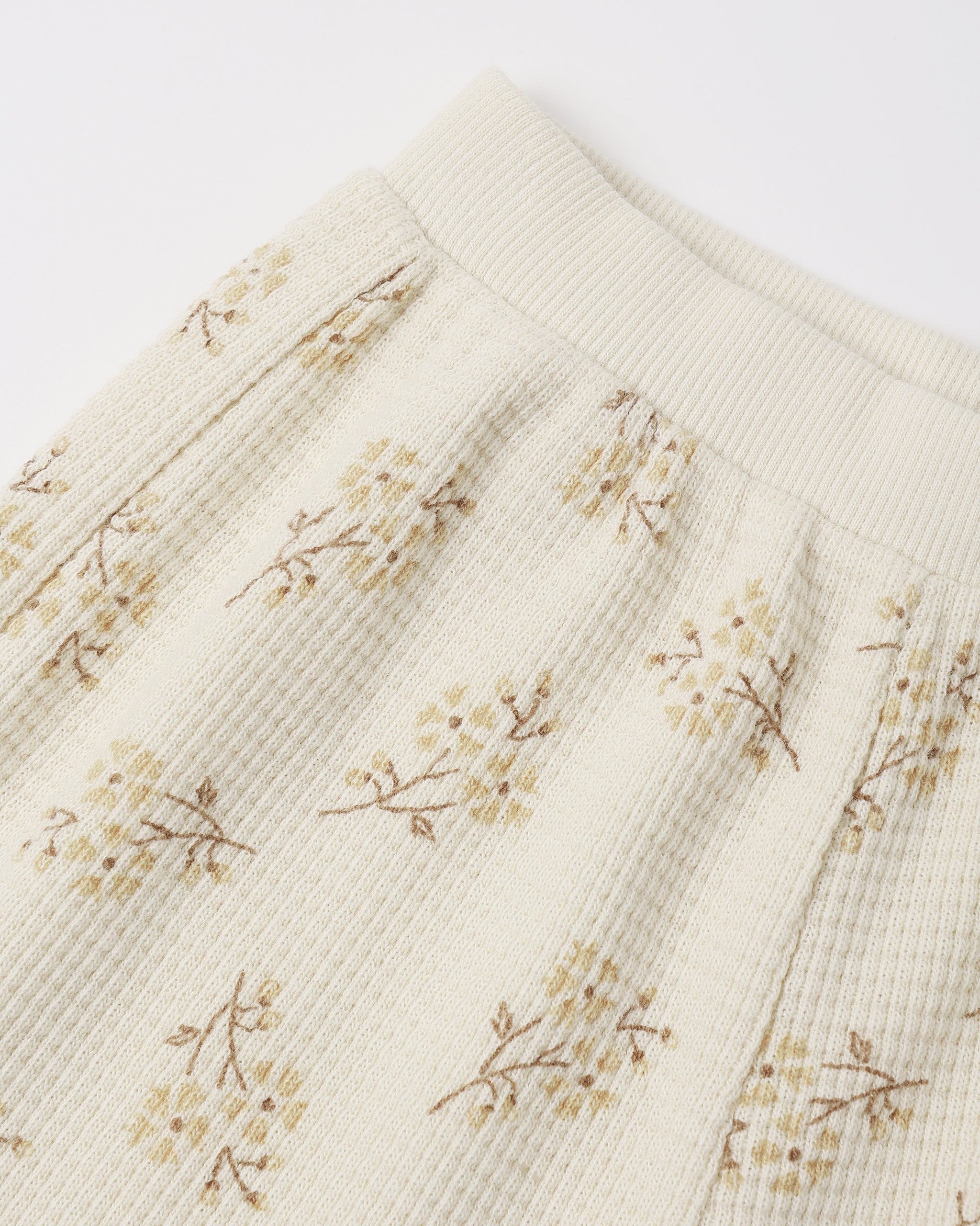 An off-white ribbed cotton toddler legging featuring a delicate, vintage-style small floral print with soft yellow and brownish stems.