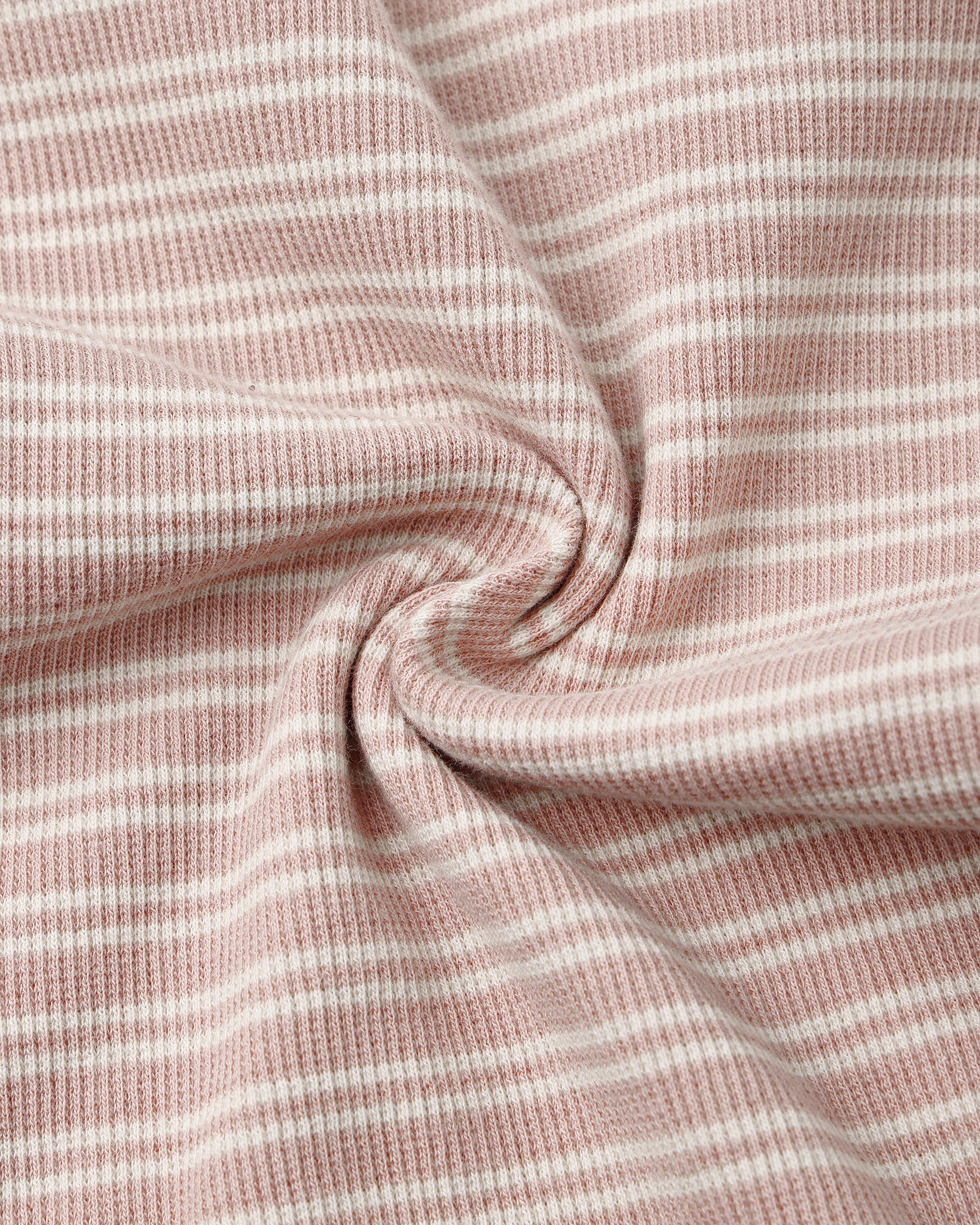 A close-up of a soft knit fabric with a dusty pink and white horizontal stripe pattern, arranged in a central swirl to highlight its texture and drape.