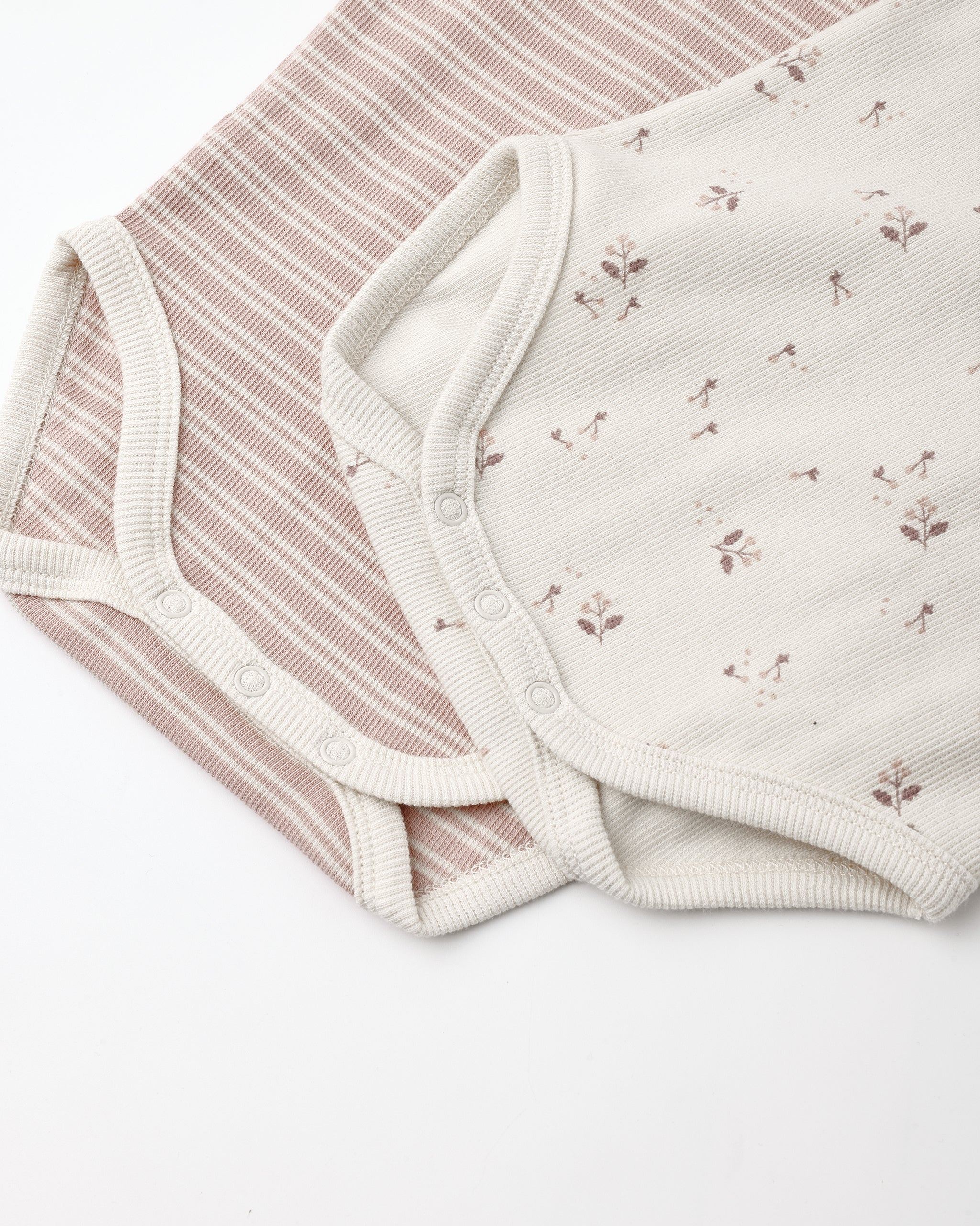 Two soft baby bodysuit fabrics laid flat on a white background: one with thin dusty pink and cream stripes, and one in warm off-white with small scattered floral motifs.