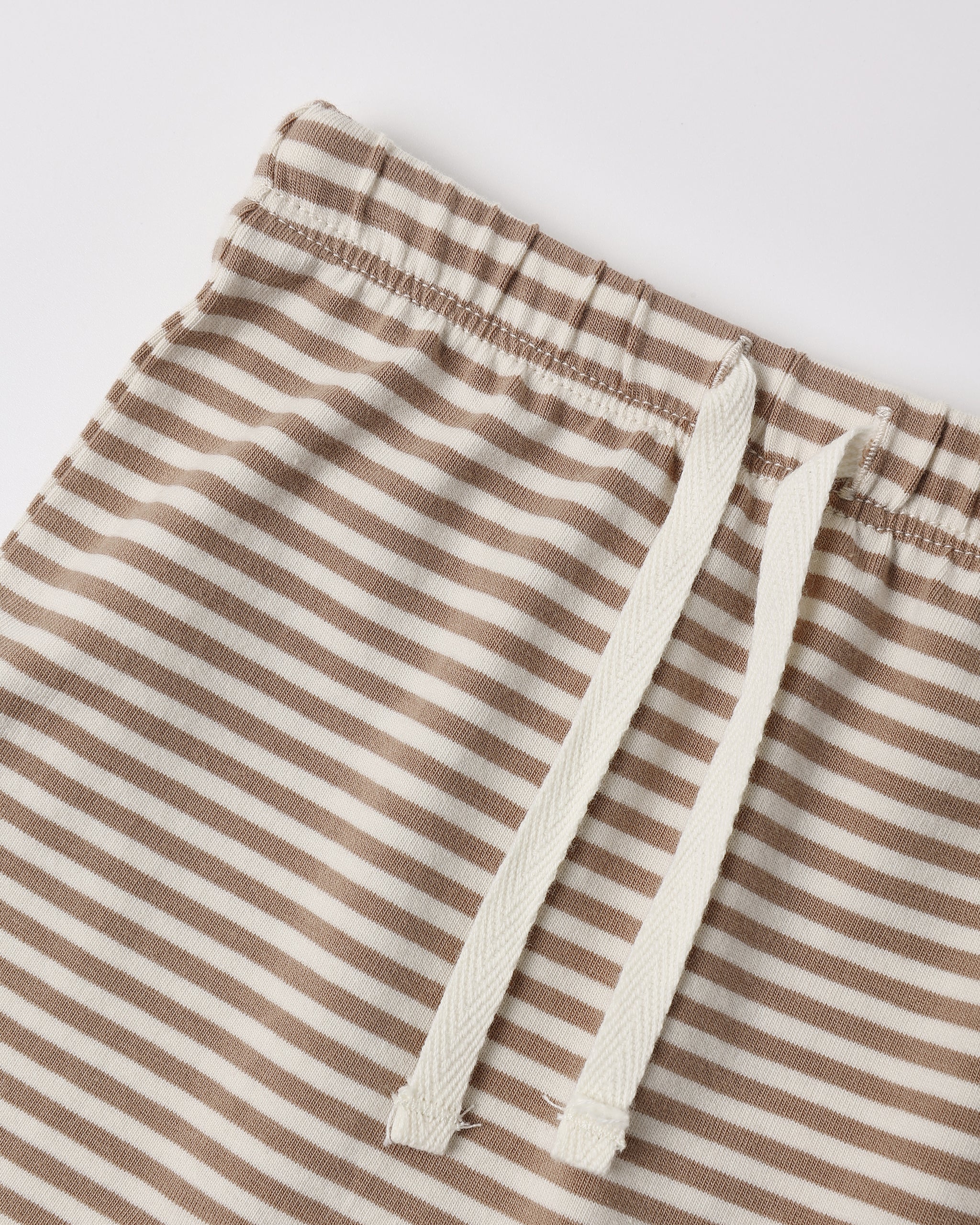 Close-up of striped drawstring shorts with a beige and off-white horizontal stripe pattern and matching off-white drawstrings, shown on a light gray background.