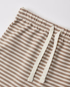 Close-up of striped drawstring shorts with a beige and off-white horizontal stripe pattern and matching off-white drawstrings, shown on a light gray background.