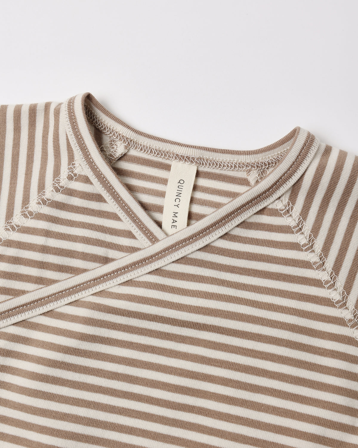 Close-up of a baby wrap top with horizontal beige and off-white stripes, featuring a V-neck and a visible 'CONCEPT MATE' brand tag.