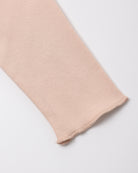 A close-up of a light blush pink knit fabric sleeve or cuff with a frayed hem, shown on a clean white background.