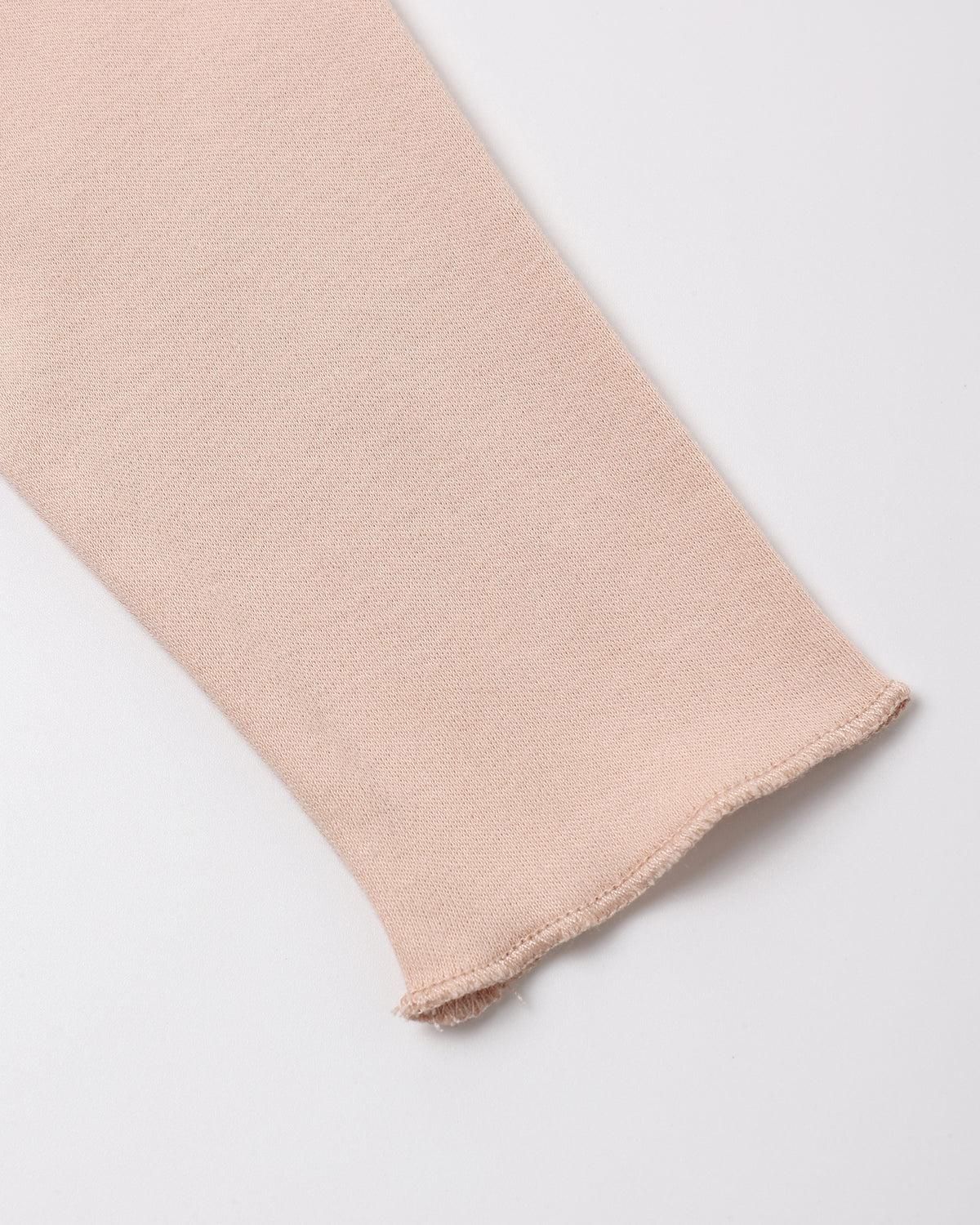 A close-up of a light blush pink knit fabric sleeve or cuff with a frayed hem, shown on a clean white background.