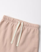 Close-up of a pair of soft blush pink sweatpants with an off-white drawstring, shown against a plain light background.