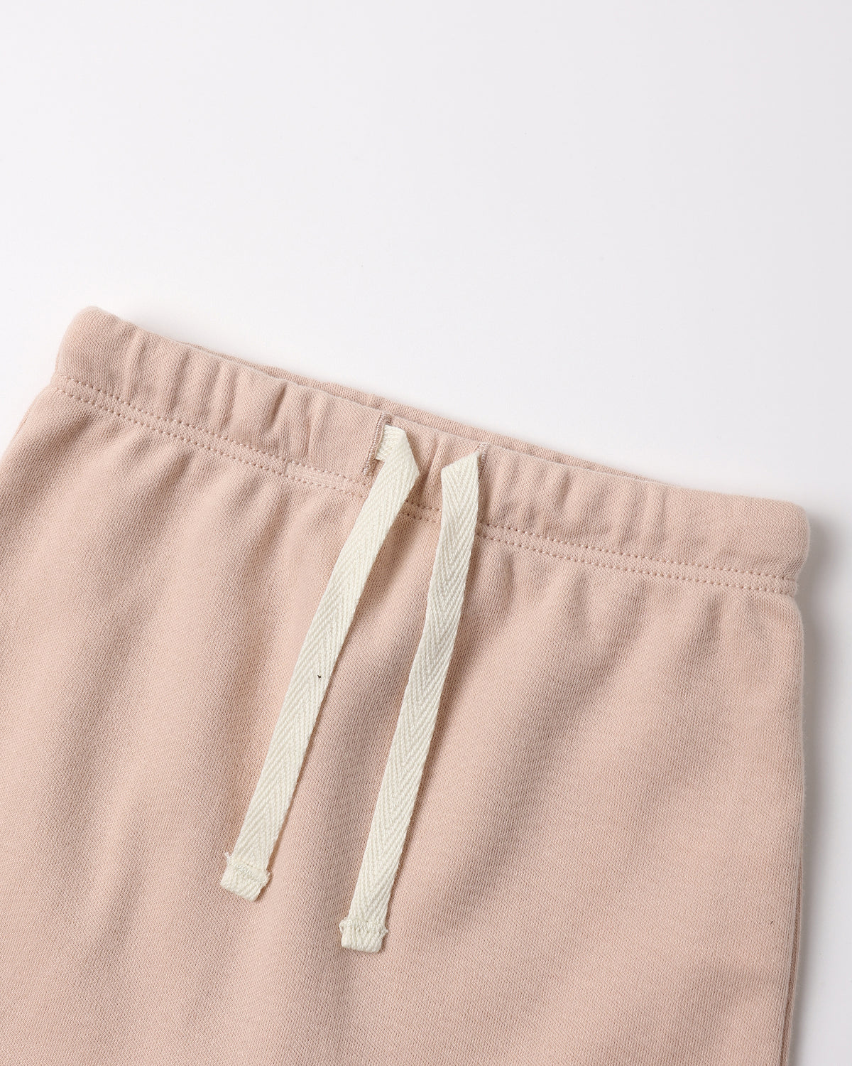 Close-up of a pair of soft blush pink sweatpants with an off-white drawstring, shown against a plain light background.