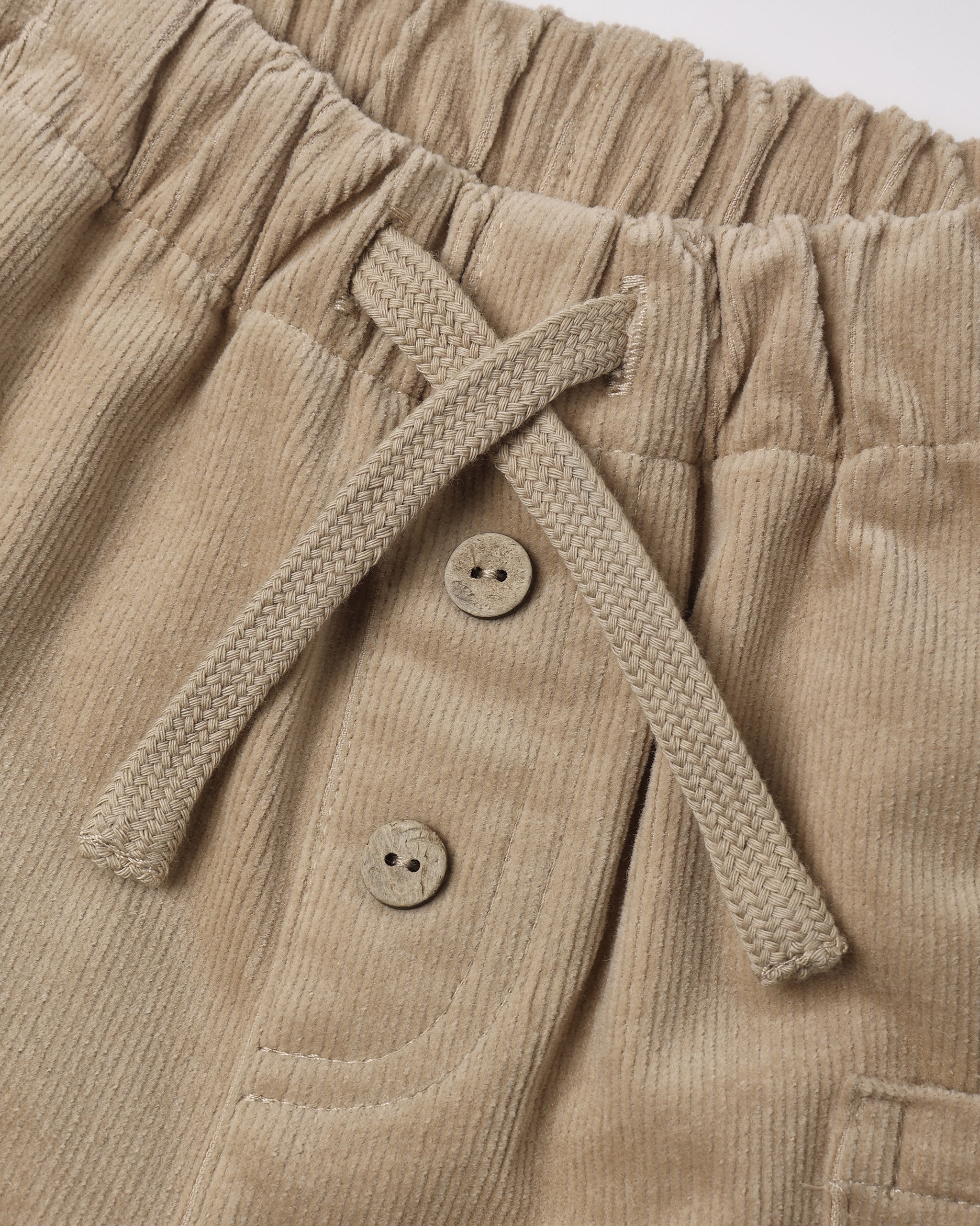 Close-up view of the Quincy Mae Luca Pant in Latte, featuring beige corduroy fabric with an elastic waistband, a tied fabric drawstring, and two decorative buttons on the front.
