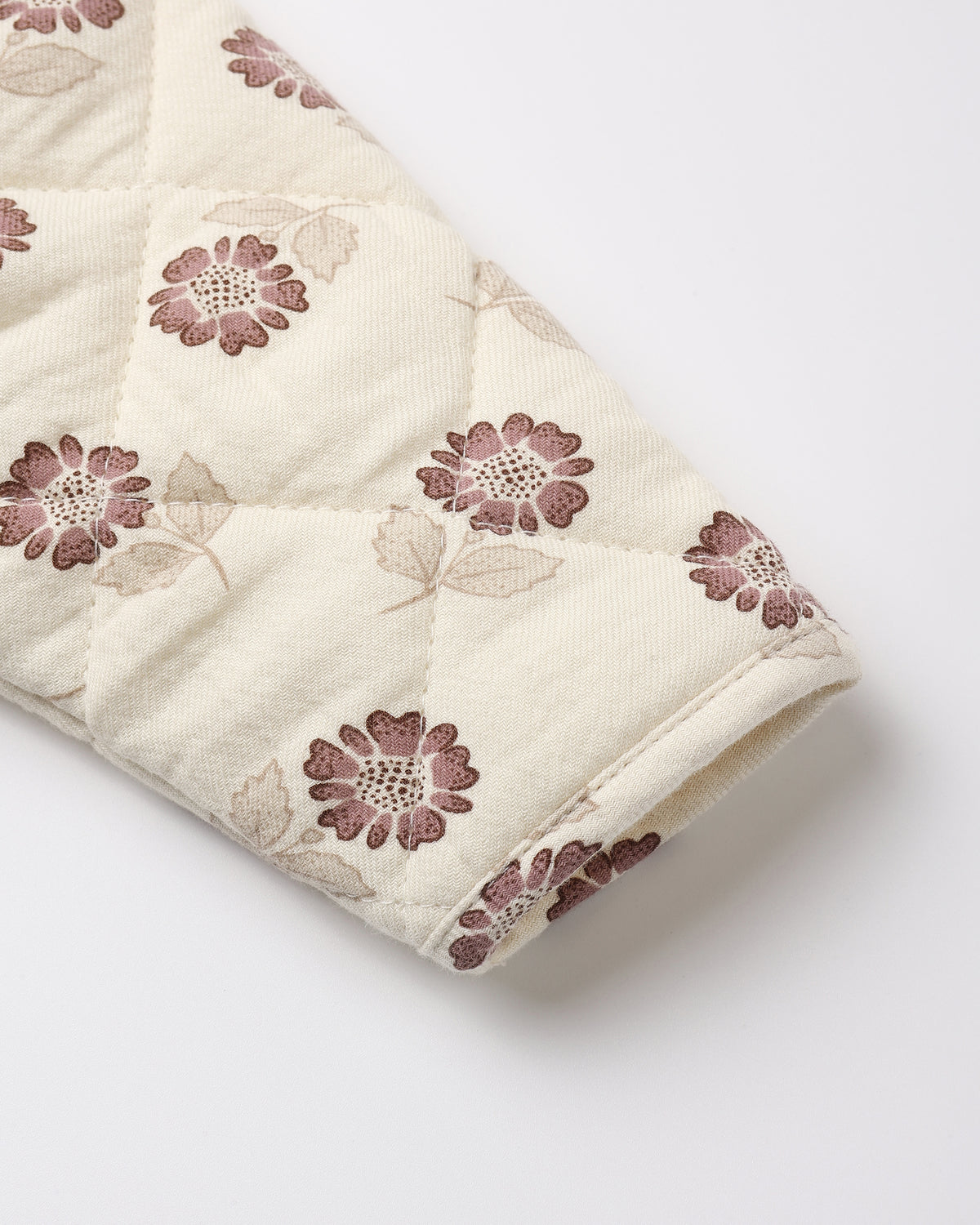 A close-up of a quilted fabric sleeve or cuff in cream with a repeating floral pattern in dusty mauve and beige, shown on a light gray background.