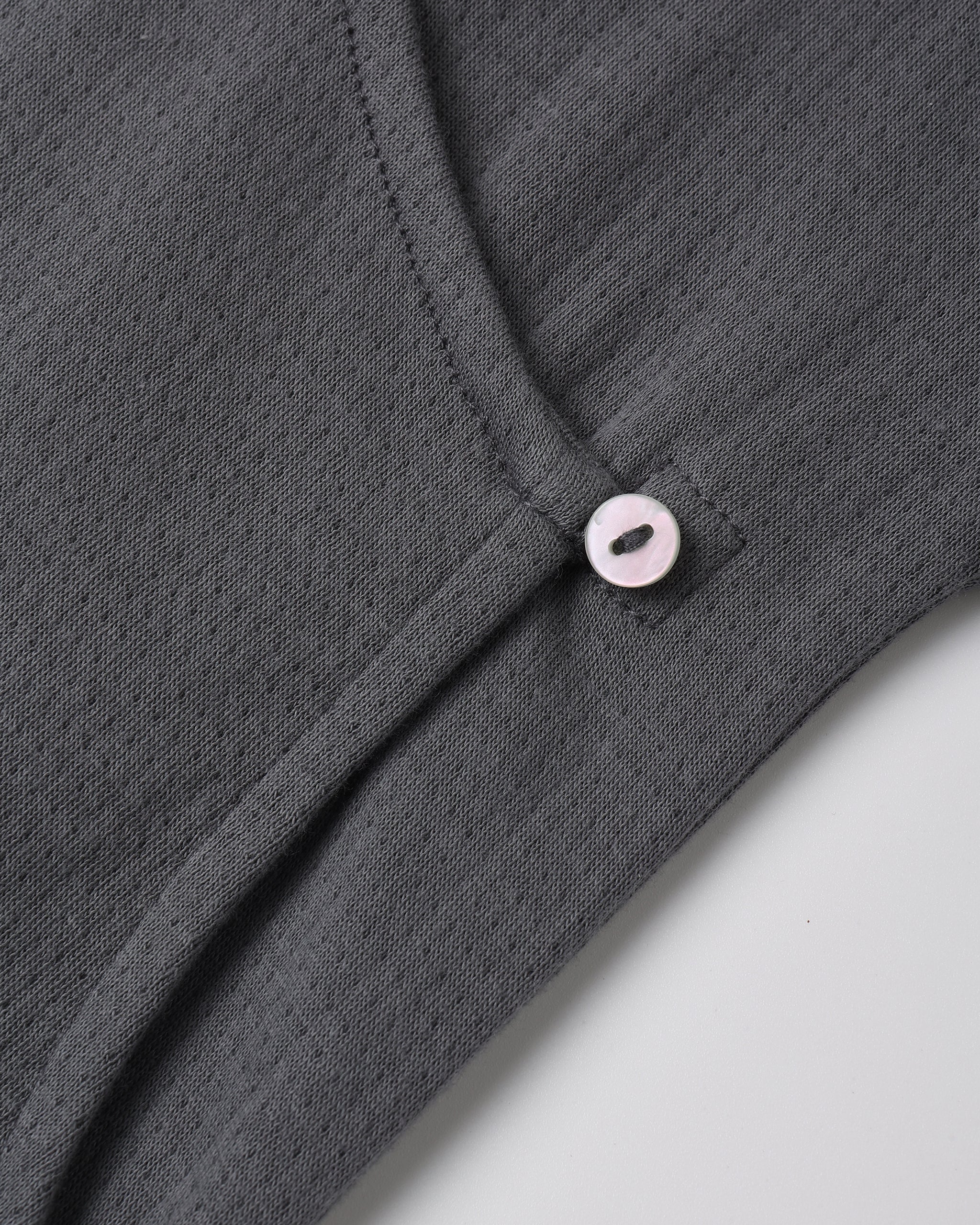 A dark grey textured knit top featuring an asymmetric neckline secured with a small light-colored button