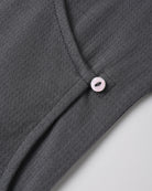 A dark grey textured knit top featuring an asymmetric neckline secured with a small light-colored button