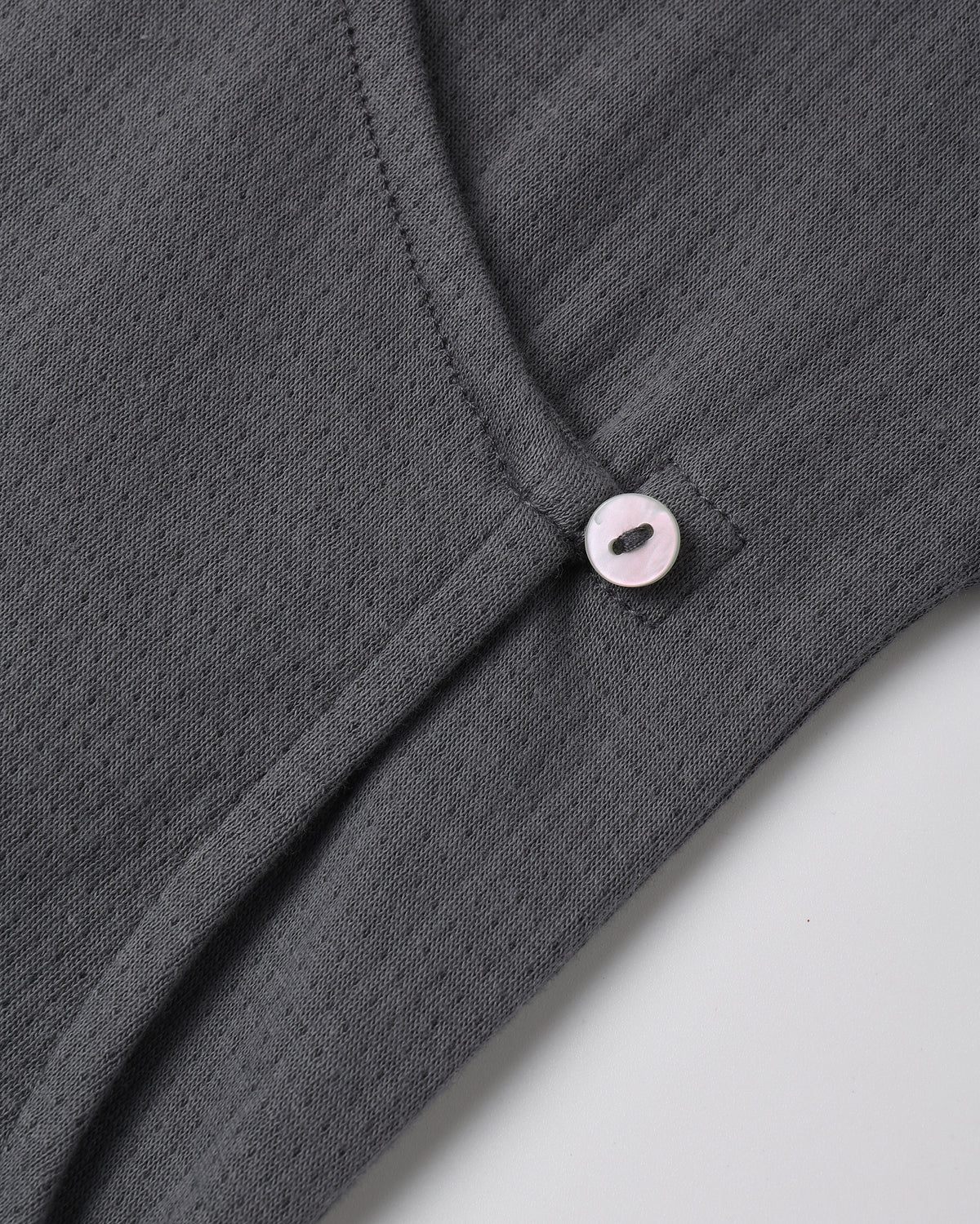 A dark grey textured knit top featuring an asymmetric neckline secured with a small light-colored button