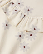 Close-up of a cream-colored fabric garment featuring a ruffled neckline and an all-over daisy print with light gray petals and dark brown centers.