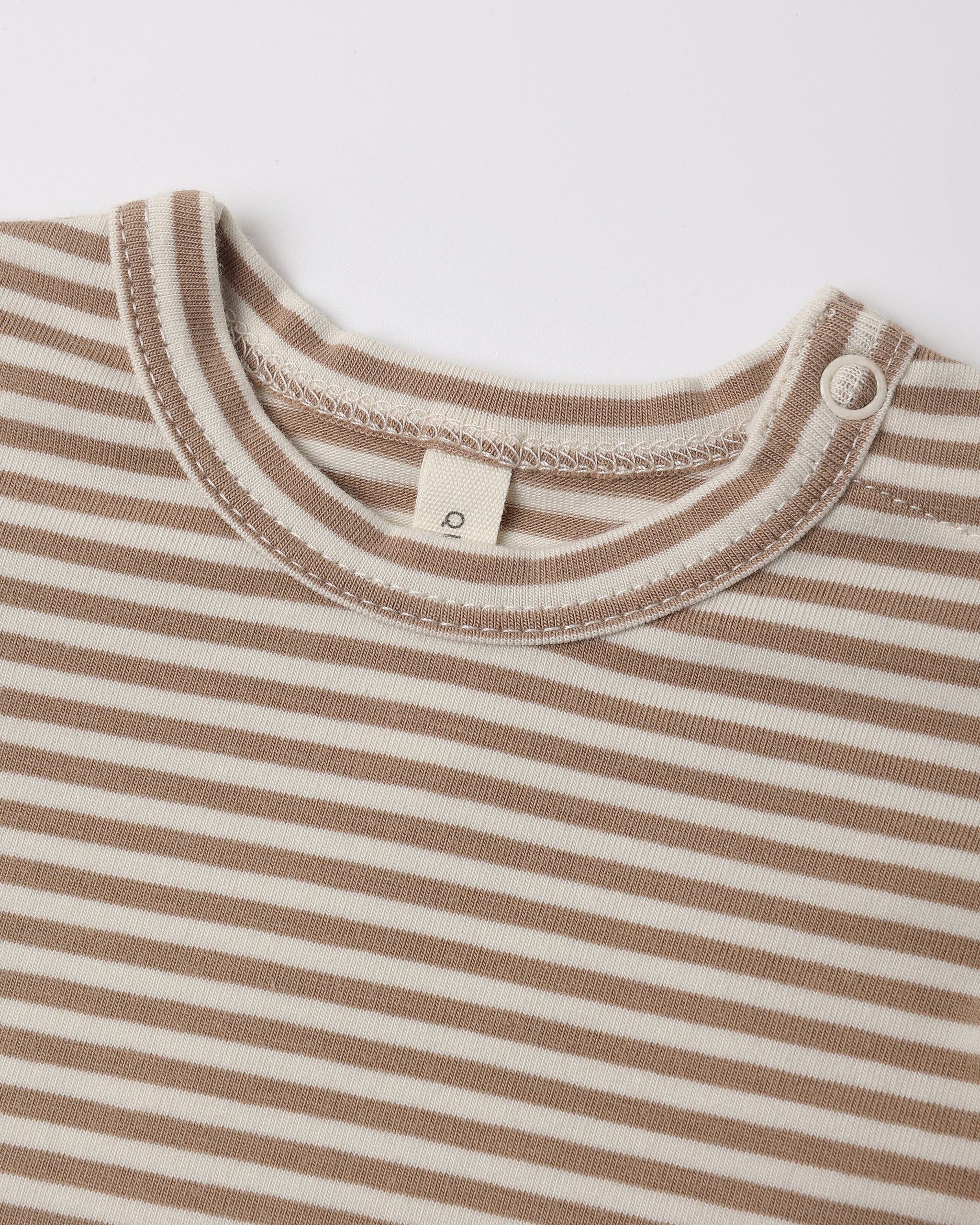 Close-up of a striped baby top with a cream and light brown horizontal stripe pattern, featuring a ribbed crew neck and a small white tag.