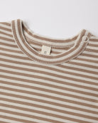 Close-up of a striped baby top with a cream and light brown horizontal stripe pattern, featuring a ribbed crew neck and a small white tag.