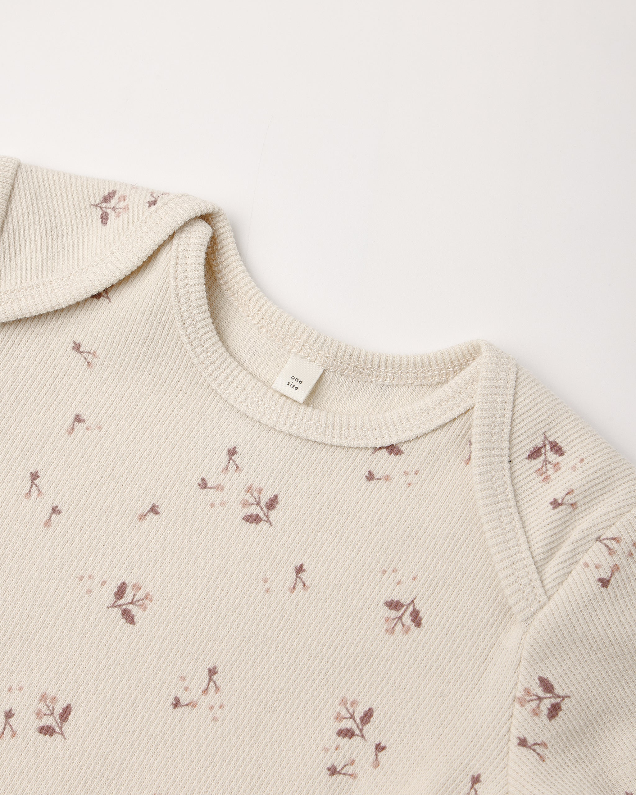 Close-up of a cream-colored ribbed knit garment, likely a baby top or sweater, featuring a delicate brown floral and leaf pattern scattered across the fabric.